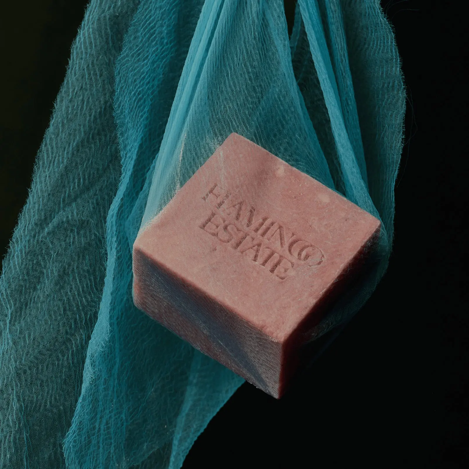 A pink Flamingo Estate soap bar on teal fabric
