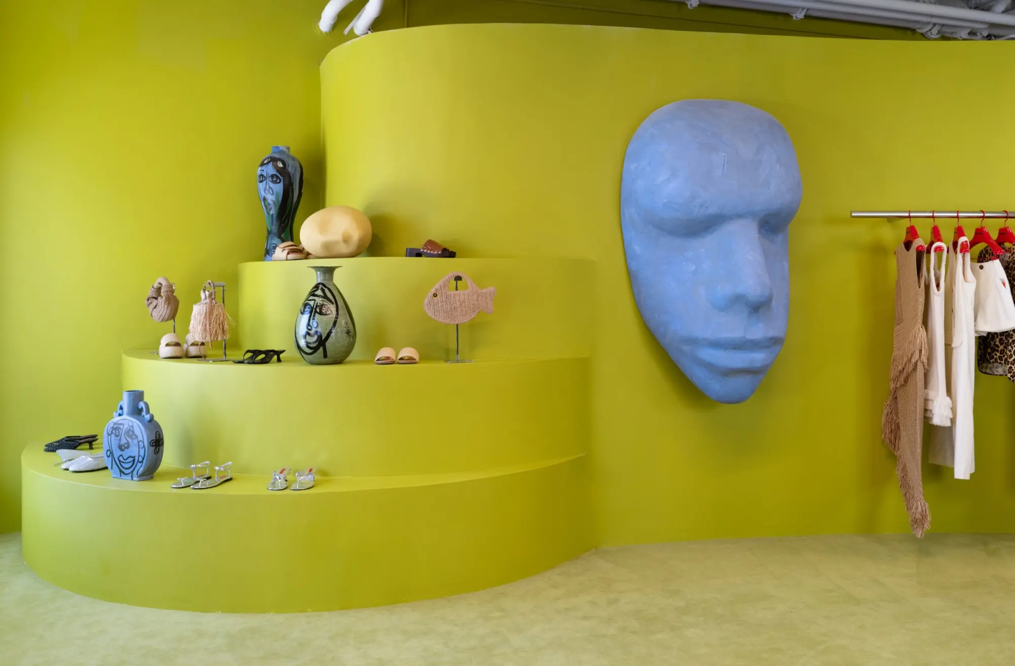 A yellow-green display with a blue face sculpture in the Simon Miller store at Signal